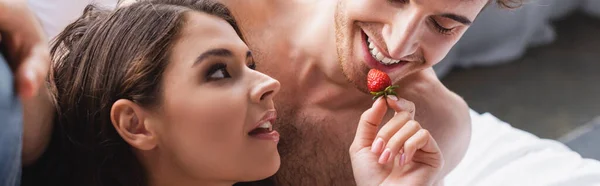 Панорамный урожай женщины, держащей клубнику и питающей мускулистого мужчину — стоковое фото