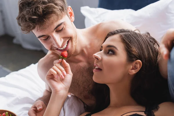 Brunette woman holding strawberry and feeding muscular man — Stock Photo