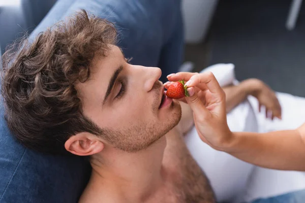 Young woman holding strawberry and feeding muscular man — Stock Photo