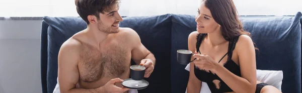 Горизонтальний урожай м'язової людини і спокусливої жінки, що тримає чашки з чаєм в ліжку — стокове фото