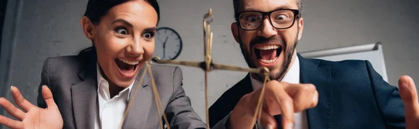 Panoramic shot of excited businessman and businesswoman in formal wear touching scales — Stock Photo