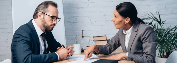 Tiro panorâmico de empresária apontando com o dedo para o documento e conversando com colega de trabalho em óculos — Fotografia de Stock