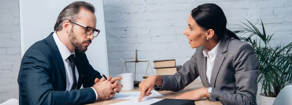 Plano panorámico de la empresaria señalando con el dedo al documento y hablando con su compañero de trabajo en gafas - foto de stock