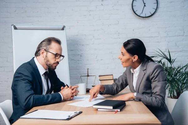 Empresaria señalando con el dedo al documento y hablando con compañero de trabajo en gafas - foto de stock