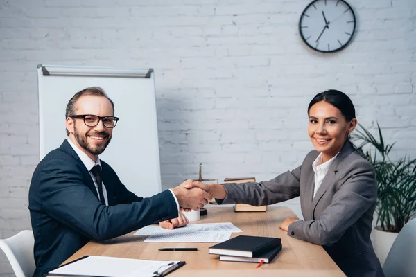 Businessman in glasses and businesswoman shaking hands near documents — Stock Photo