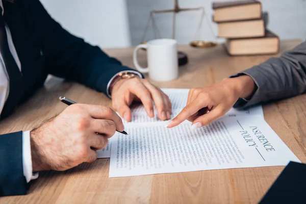 Vue recadrée de l'avocat pointant du doigt le contrat de police d'assurance près de l'homme d'affaires avec stylo — Photo de stock