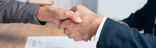 Panoramic crop of businessman and businesswoman shaking hands in office — Stock Photo