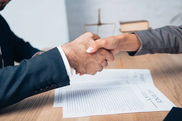 Cropped view of businessman and businesswoman shaking hands near documents — Stock Photo