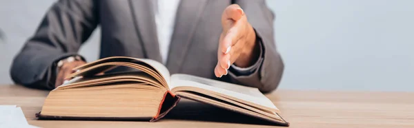 Panoramic crop of lawyer in suit pointing with hand at book in office — Stock Photo