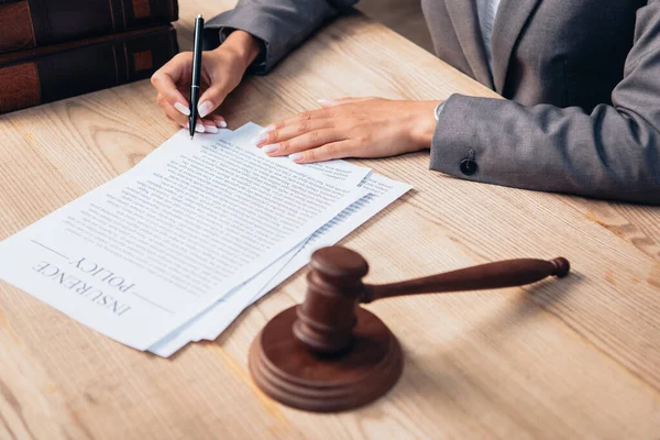 Cropped view of judge signing insurance policy document near gavel in office — Stock Photo