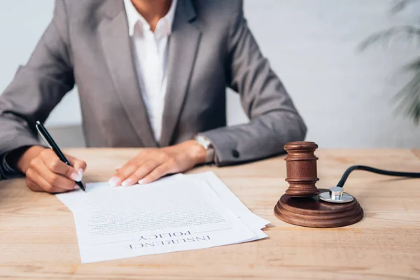 Cropped view of judge signing insurance policy contract near gavel and stethoscope — Stock Photo