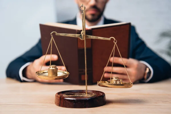 Cropped view of bearded lawyer reading book near golden scales on table — Stock Photo