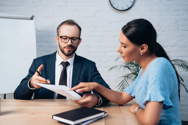 Selective focus of woman pointing with finger at document near bearded lawyer in glasses — Stock Photo