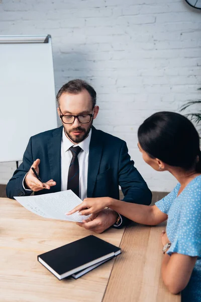 Selective focus of client pointing with finger at document near bearded lawyer in glasses — Stock Photo