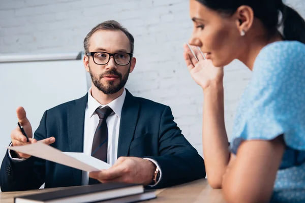 Accent sélectif de barbu avocat dans des lunettes regardant le client tout en tenant le document en fonction — Photo de stock