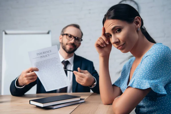 Selektiver Fokus des unzufriedenen Kunden, der in die Kamera neben dem bärtigen Anwalt mit der Brille blickt, der den Versicherungsvertrag hält — Stockfoto