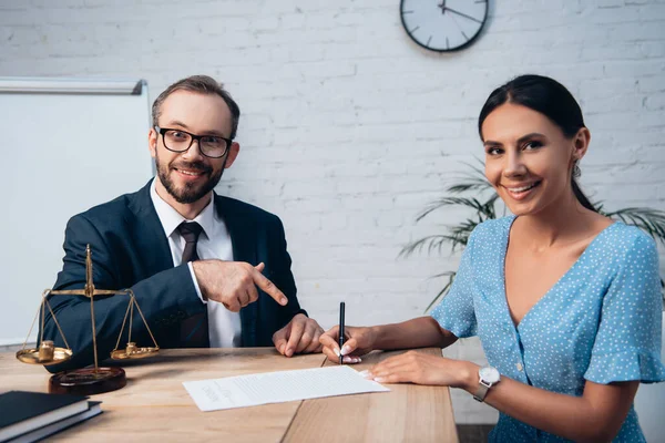 Избирательный фокус юриста в очках, указывающий пальцем на подписание клиентом договора страхования в офисе — стоковое фото