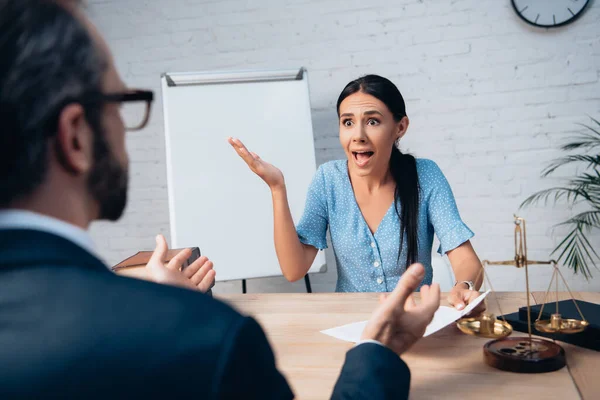 Selective focus of brunette client screaming and gesturing while holding contract near lawyer in office — Stock Photo