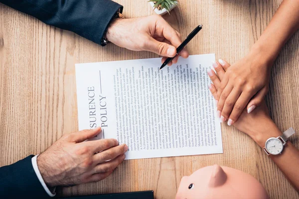 Top view of lawyer holding pen near insurance policy agreement, piggy bank, plant and woman — Stock Photo