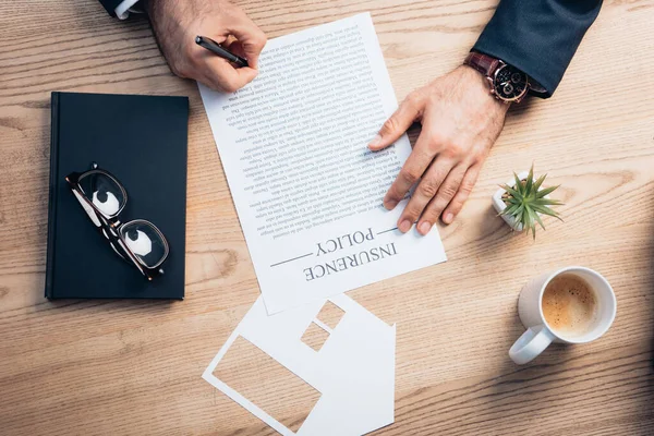 Top view of lawyer signing insurance policy agreement near plant, glasses, notebook and paper cup house model — Stock Photo