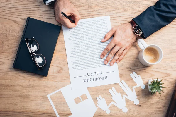 Top view of lawyer signing insurance policy contract near plant, glasses, notebook and paper cup house model with family — Stock Photo