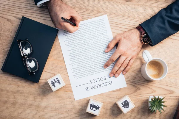 Top view of lawyer signing insurance policy agreement near plant, glasses, notebook and wooden cubes with family, car and house — Stock Photo