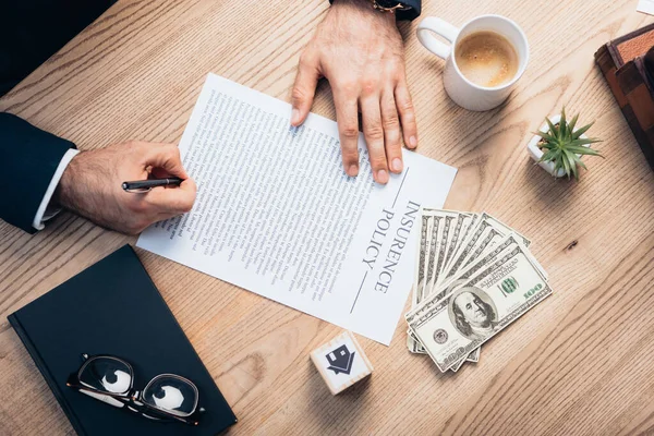 Top view of lawyer signing insurance policy agreement near plant, glasses, notebook, dollars and cube with house — Stock Photo