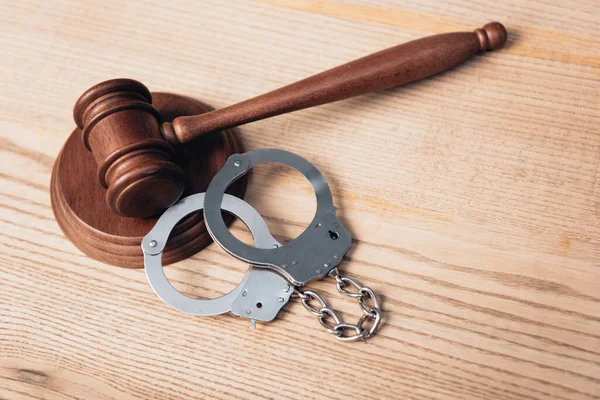 Gavel near metallic handcuffs on wooden desk — Stock Photo