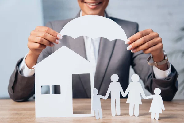 Abgeschnittene Ansicht eines Rechtsanwalts, der einen papiergeschnittenen Regenschirm in der Nähe von dekorativen Haus- und Familienelementen hält — Stockfoto