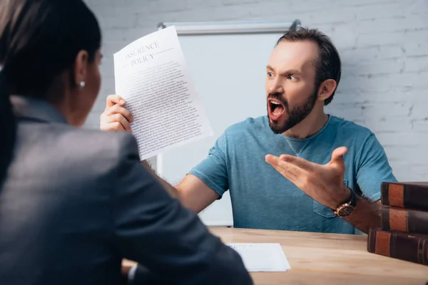 Selective focus of angry and bearded man screaming while holding insurance policy agreement near lawyer — Stock Photo