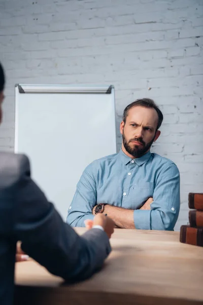 Selektiver Fokus des unzufriedenen Mandanten, der mit verschränkten Armen neben dem Anwalt sitzt — Stockfoto