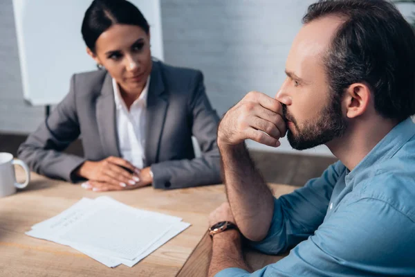 Selective focus of pensive man touching face near brunette lawyer and documents on table — Stock Photo