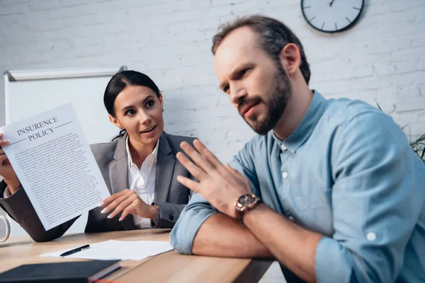 Selective focus of brunette lawyer holding insurance policy agreement near bearded man showing no gesture — Stock Photo