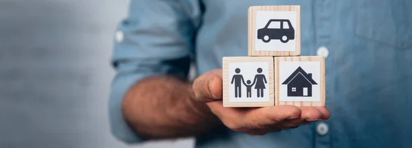 Panoramic crop of man holding wooden cubes with car, family and house — Stock Photo