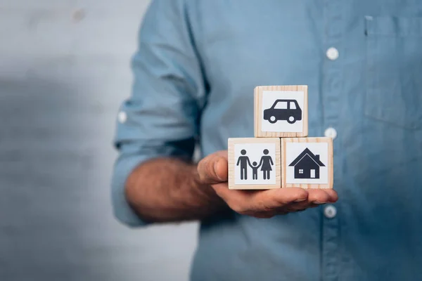 Vista recortada del hombre sosteniendo cubos de madera con coche, familia y casa en la mano - foto de stock