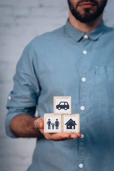 Обрізаний вид бородатого чоловіка, який тримає дерев'яні кубики з машиною, сім'єю та будинком в руці — стокове фото