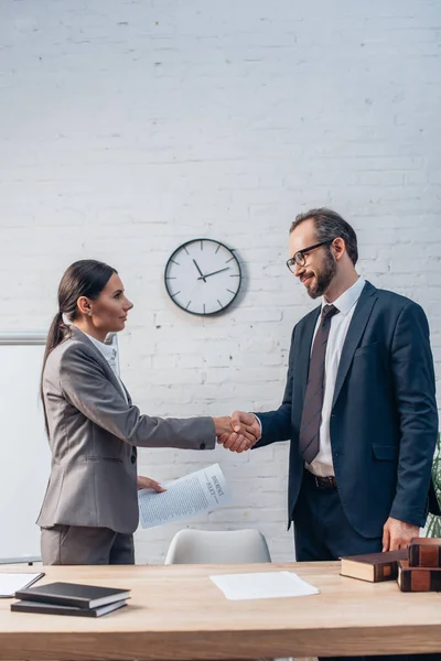 Juristen in offizieller Kleidung geben sich in der Nähe von Dokumenten im Amt die Hand — Stockfoto