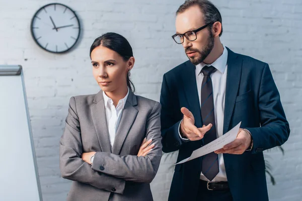 Lawyer in glasses pointing with finger at insurance document and looking at businesswoman with crossed arms — Stock Photo