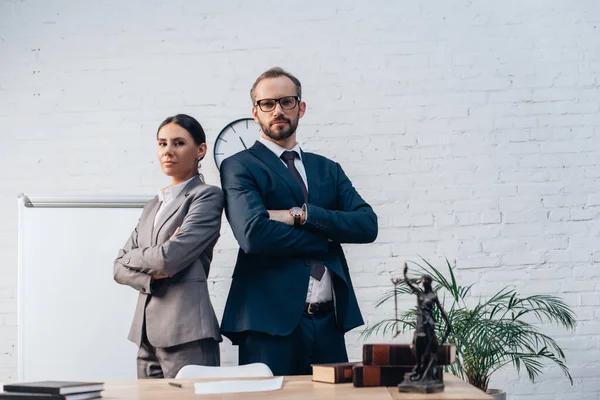Confident lawyers in suits standing with crossed arms and looking at camera in office — Stock Photo