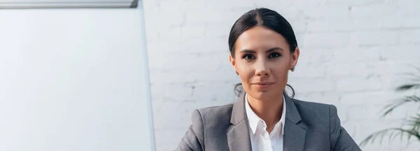 Panoramic crop of brunette lawyer in formal wear looking at camera in office — Stock Photo