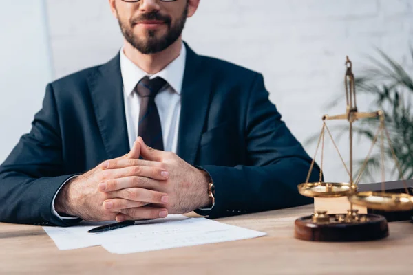 Cropped view of bearded lawyer sitting with clenched hands at desk — Stock Photo