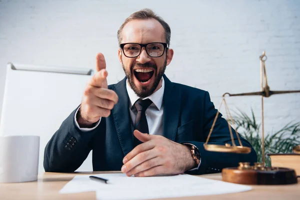 Selective focus of excited and bearded lawyer pointing with finger near scales — Stock Photo