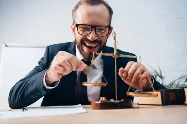 Selective focus of excited lawyer holding miniature weights near golden scales — Stock Photo