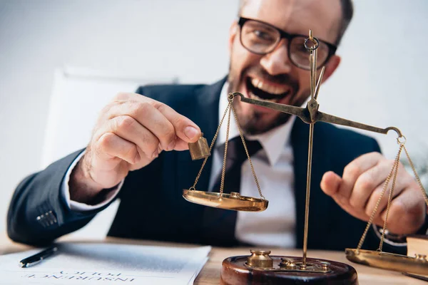 Foco seletivo de advogado animado em óculos segurando pesos em miniatura perto de escalas douradas — Fotografia de Stock