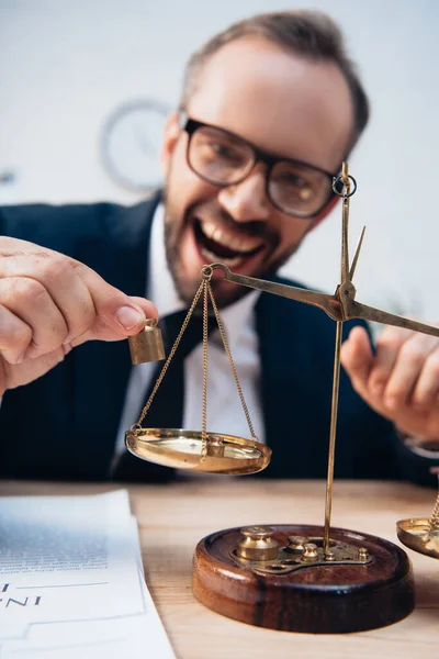 Selective focus of excited lawyer in glasses holding miniature weights near scales — Stock Photo