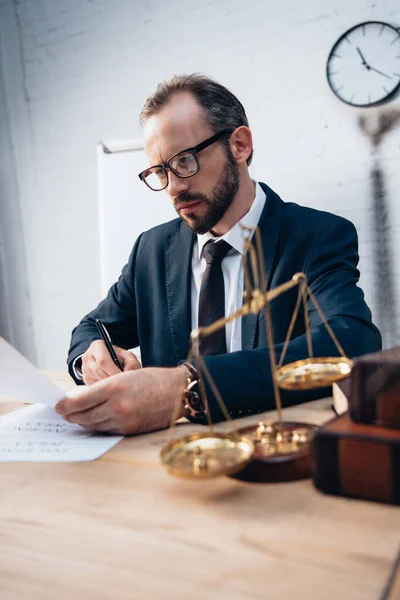 Selektiver Fokus des bärtigen Anwalts beim Signieren von Versicherungsdokumenten in der Nähe von Goldwaagen und Büchern — Stockfoto