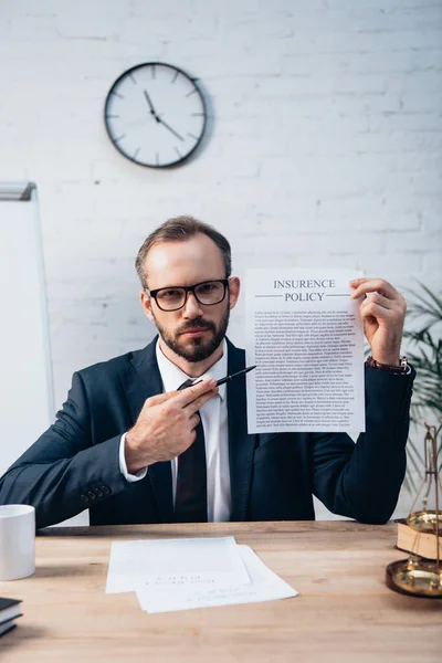 Selektiver Fokus des bärtigen Anwalts, der Stift und Vertrag mit dem Schriftzug der Versicherungspolice in die Kamera hält — Stockfoto