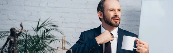 Anwalt im Anzug berührt Krawatte, während er Tasse hält — Stockfoto
