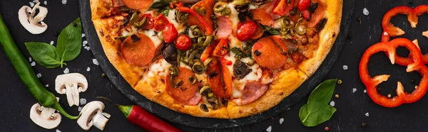 Top view of delicious Italian pizza with vegetables and salami on black background, panoramic shot — Stock Photo