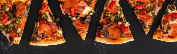 Vue de dessus de délicieuses tranches de pizza italienne avec des légumes et du salami sur fond noir, panoramique — Photo de stock